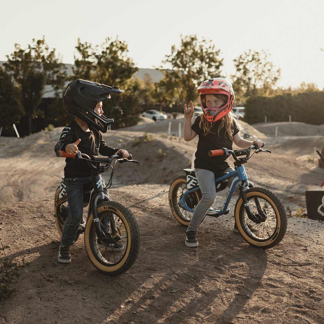 Two young riders on their blue and black SUPER73 K1D kid's e bikes sitting on a dirt track 