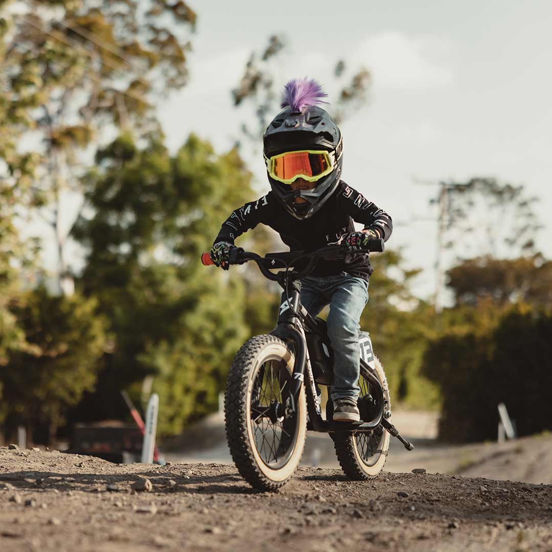 Young rider on his black SUPER73 K1D kid's e bike on a dirt track charging toward the camera with a helmet with a purple mohawk on it