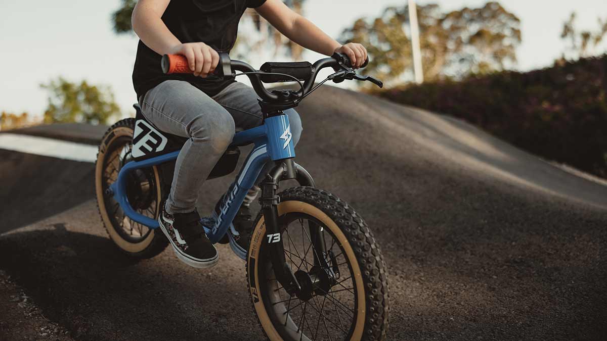 Young rider on her blue SUPER73 K1D kid's e bike on a paved pump track riding downhill