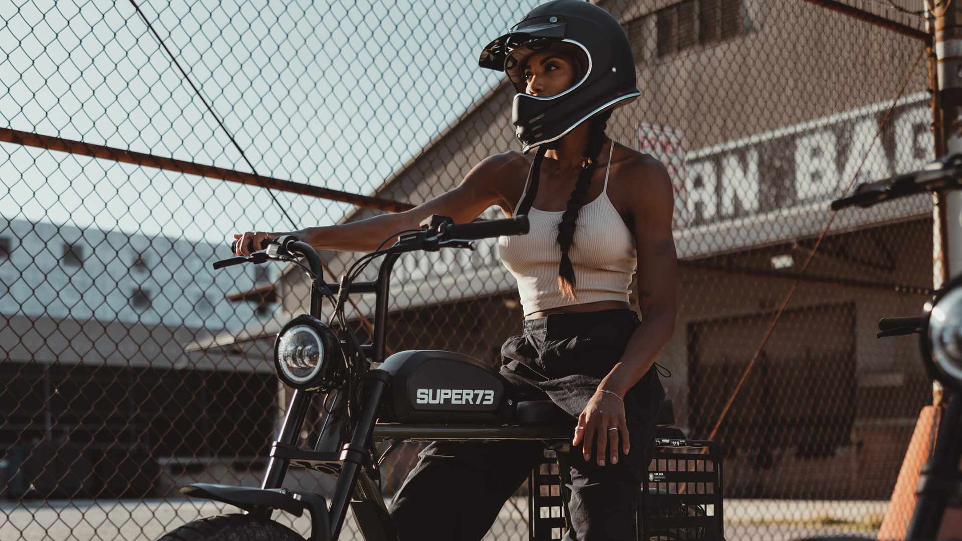 Rider sitting on Super73 S2 ebike with accessories next to chainlink fence