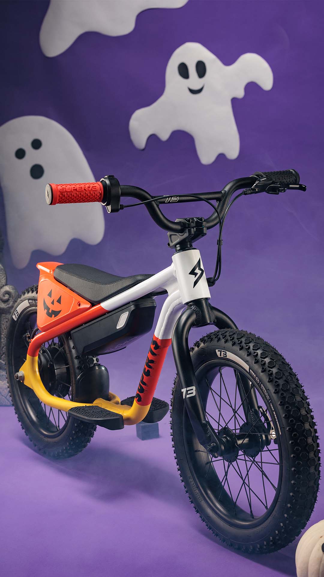 The SUPER73-K1D Candy Corn Cruise on a purple backdrop with pumpkins and ghosts in the background.