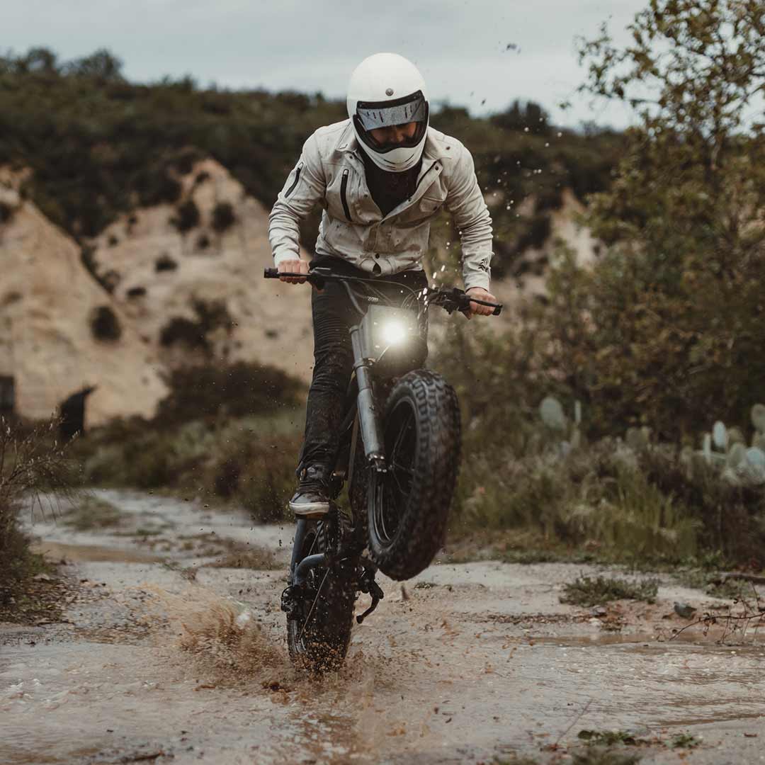Lifestyle image of a rider riding the S Adventure through mud and popping a wheelie while wearing a helmet.