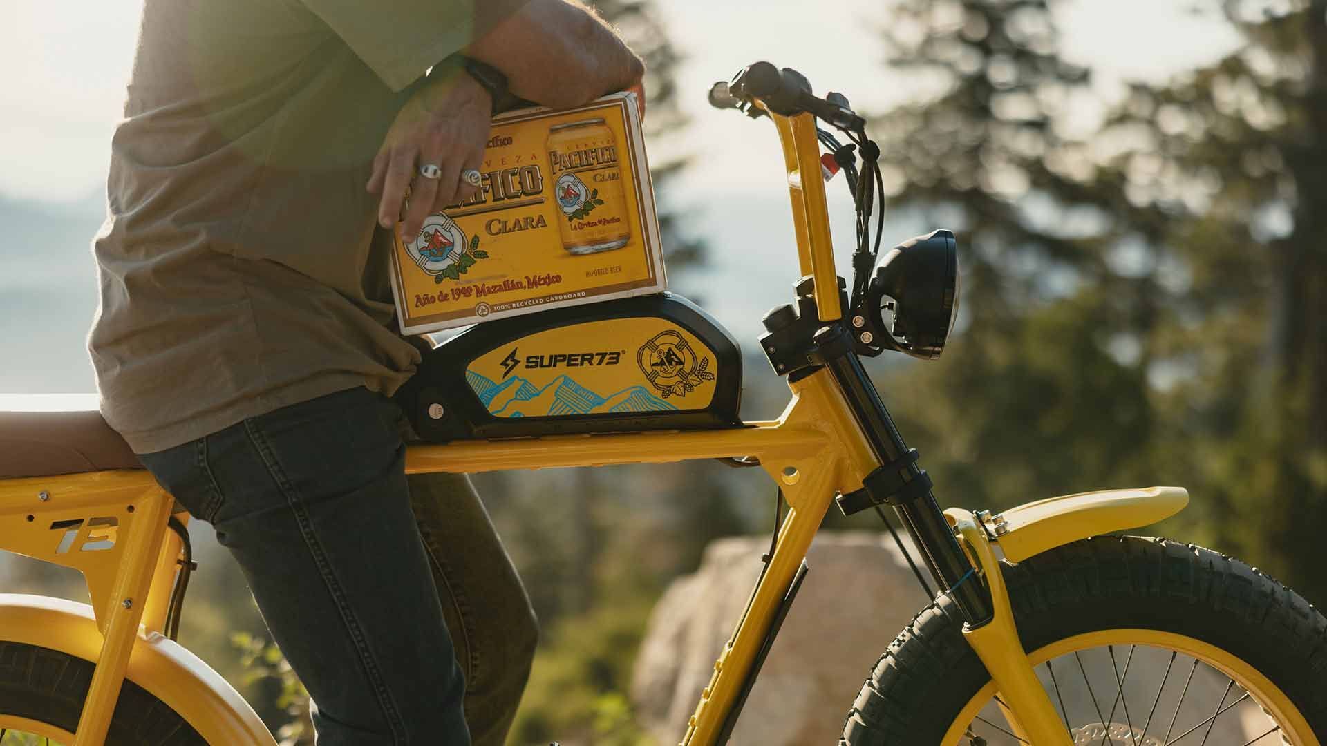 A man sits on a custom Pacifico x SUPER73-S2 bike holding a case of Pacifico beer.