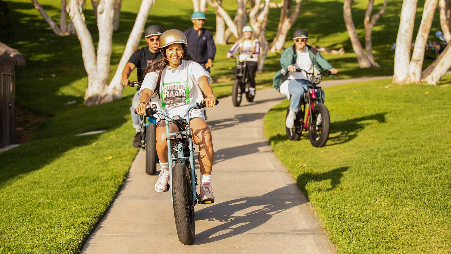 A group of friends riding ebikes down the sidewalk with helmets on.