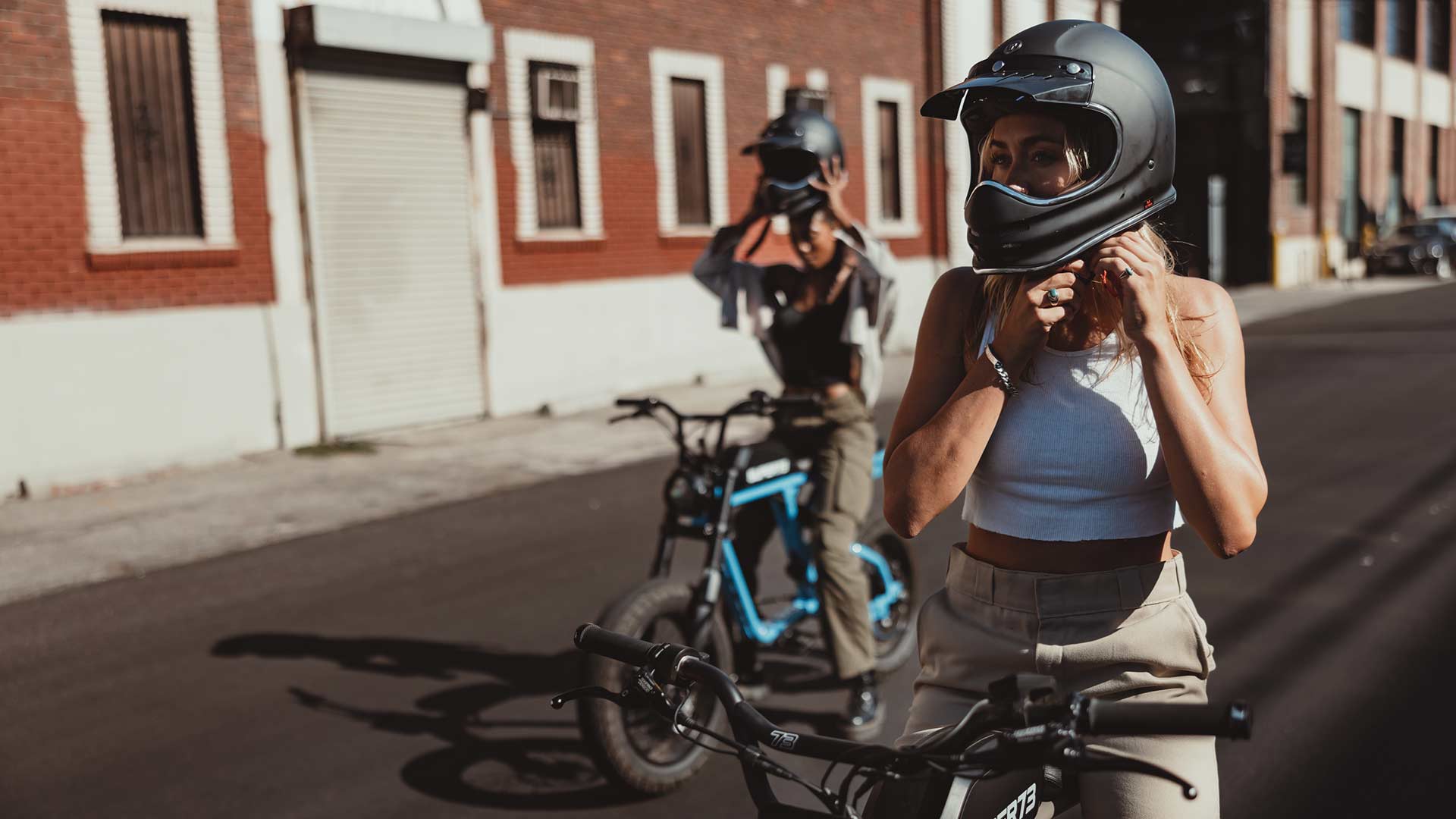 Two young girls sitting on Super73 ebikes and strapping helmets on