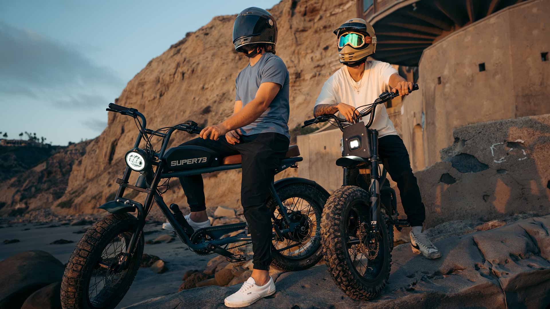 Two riders watching the sunset on their SUPER73 e-bikes on a cliff.