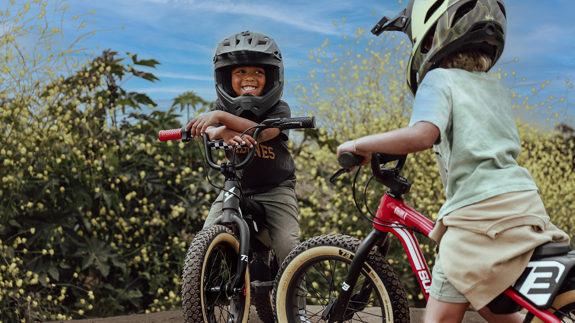 Lifestyle image of 2 young children wearing helmets on their SUPER73-K1D ebikes