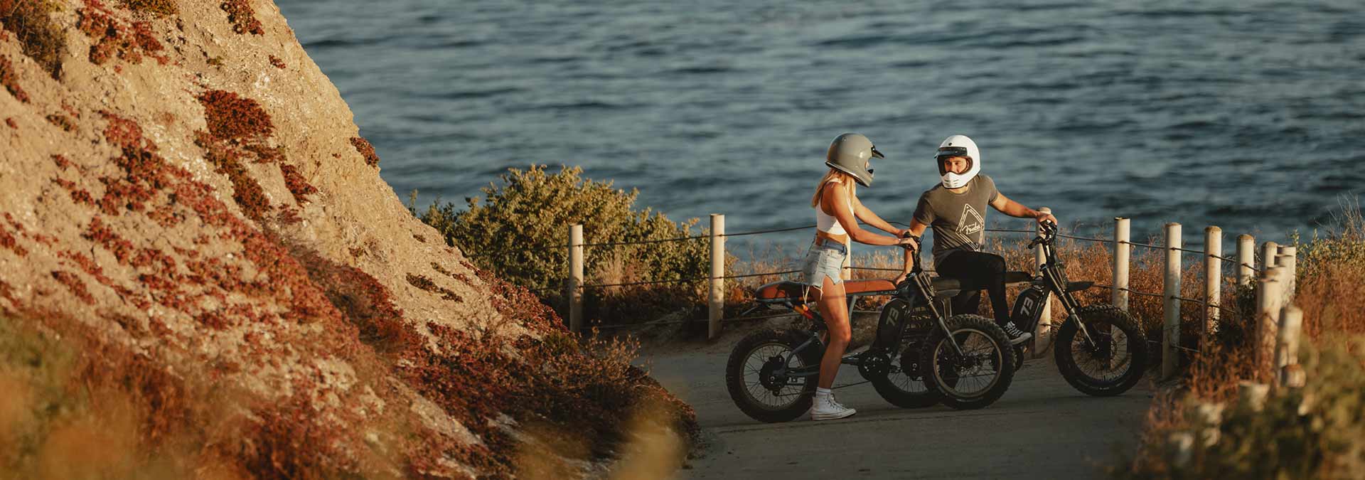 Two riders sitting on SUPER73 ebikes on the street in front of the ocean