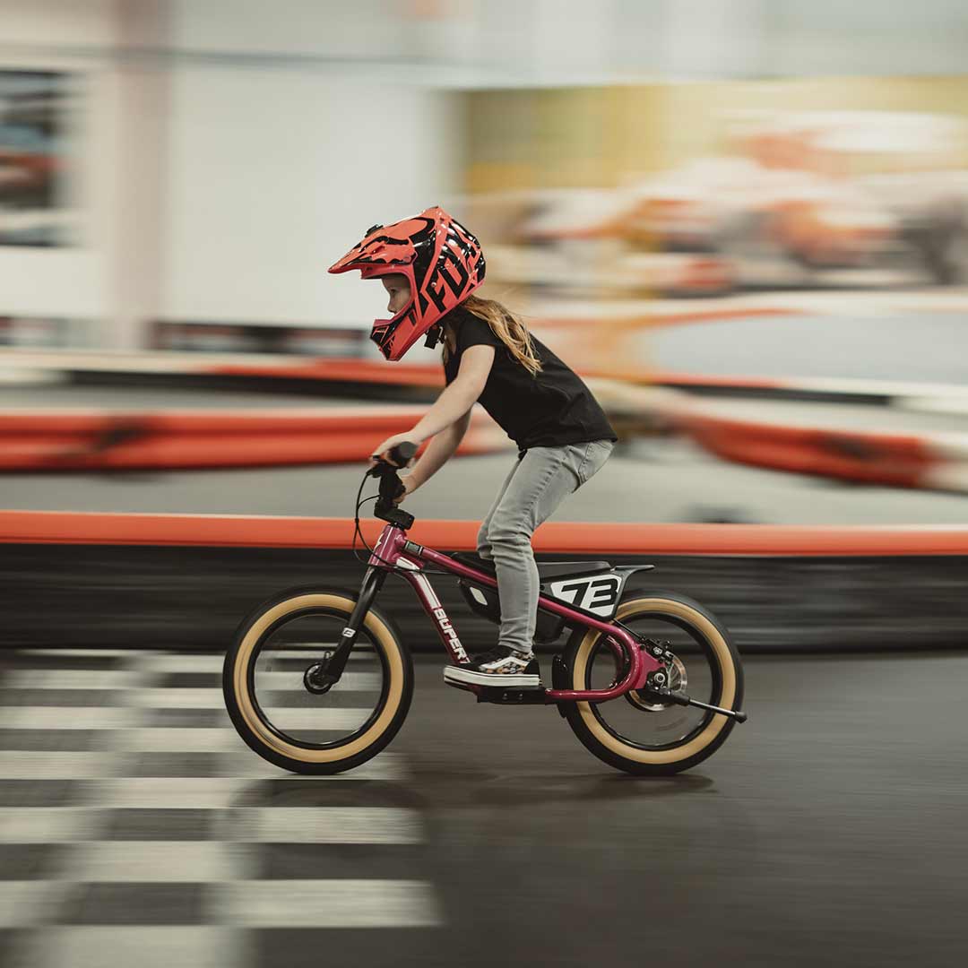 Young rider on her pink SUPER73 K1D kid's e bike on an indoor paved go kart track 