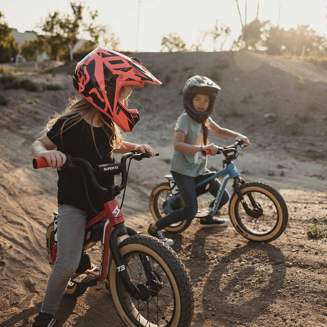 Two young riders on their SUPER73 K1D kid's e bikes on a dirt track looking at each other