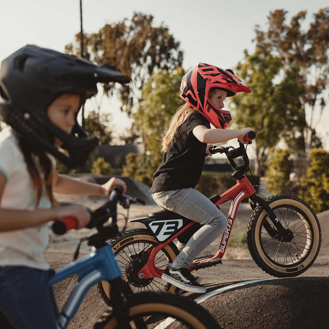 Two young riders on their blue and red SUPER73 K1D kid's e bikes on a paved pump track 