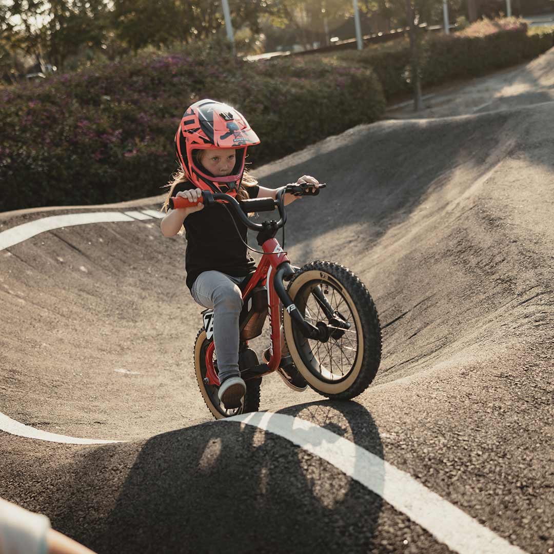 Young rider on her red SUPER73 K1D kid's e bike on a paved pump track coming up an incline
