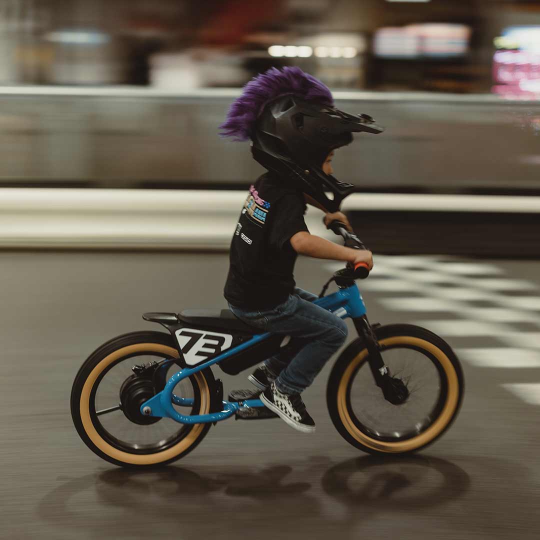 Young rider on his blue SUPER73 K1D kid's e bike on an indoor paved go kart track 