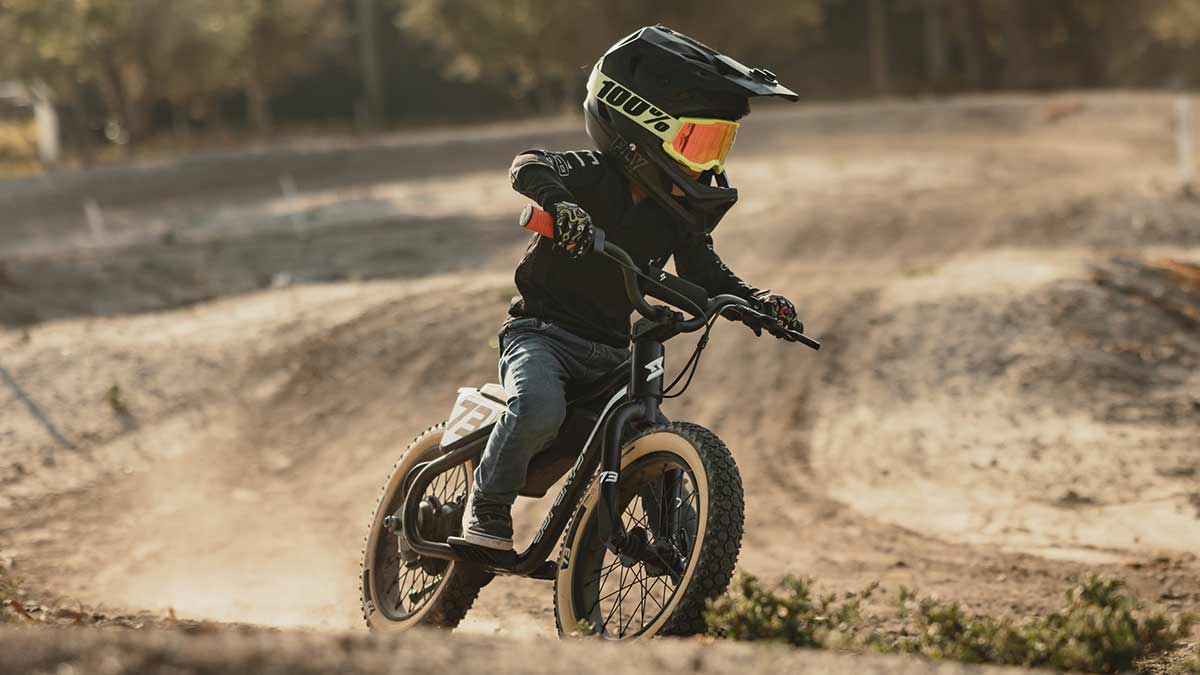 Young rider on his black SUPER73 K1D kid's ebike on a dirt track coming aggressively around a corner
