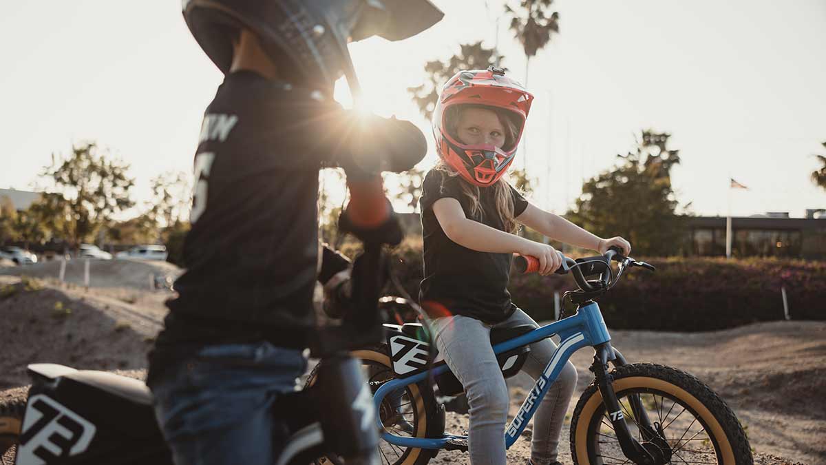 Two young riders on their SUPER73 K1D e bikes sitting on a dirt track looking at each other 