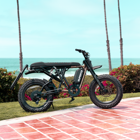 A SUPER73-R Adventure Series sits parked on a grassy area near the beach. A MBB Dual Sport Surf Rack is installed on the bike.