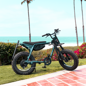 A SUPER73-Z Adventure Series sits parked on a grassy area near the beach. A MBB Dual Sport Surf Rack is installed on the bike.