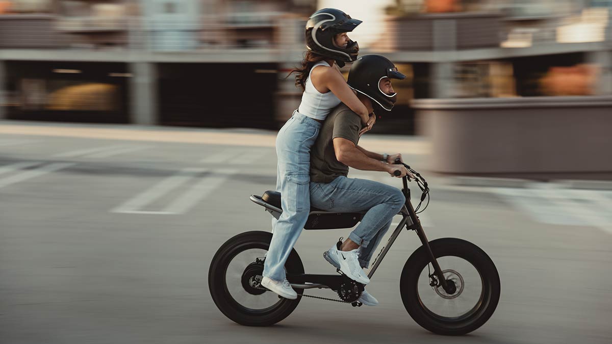 Young man riding a SUPER73 Z Series ebike with a young lady on the back standing on footpegs.