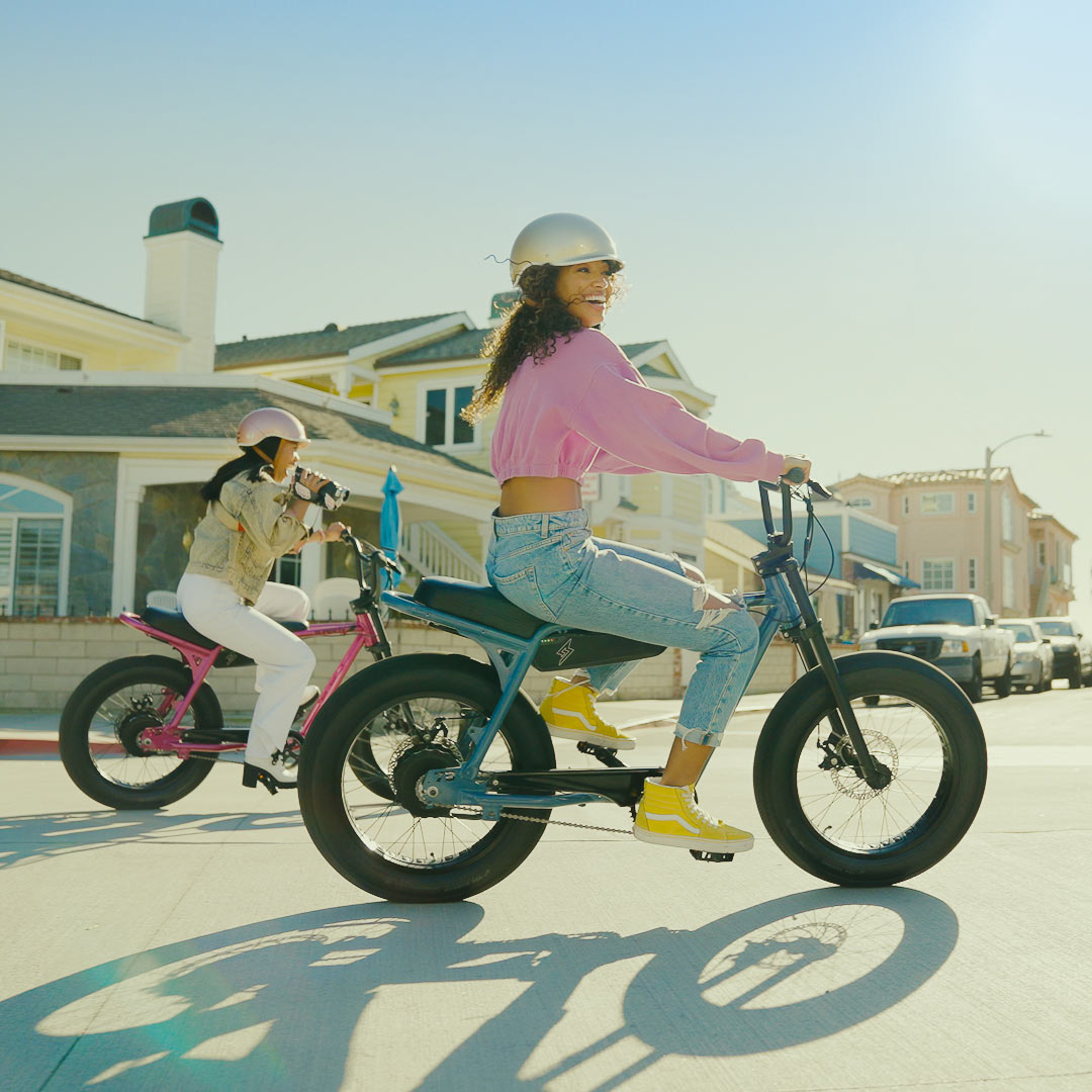 Lifestyle image of two young women riding SUPER73-Z Miami ebikes in Panthro Blue and Prickly Pink
