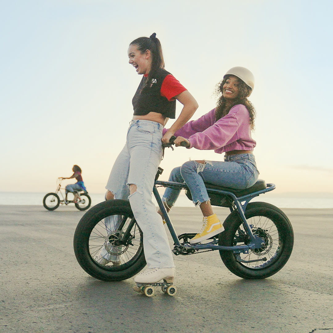 Lifestyle image of a young woman riding a SUPER73-Z Miami ebike in Panthro Blue and another young woman on rollerskates.