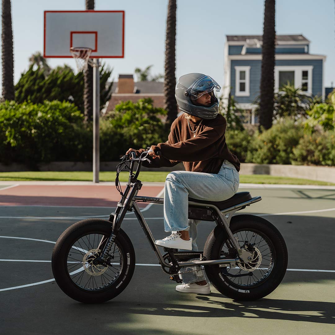 A woman sits atop a SUPER73-Z Miami SE bike on a basketball court.