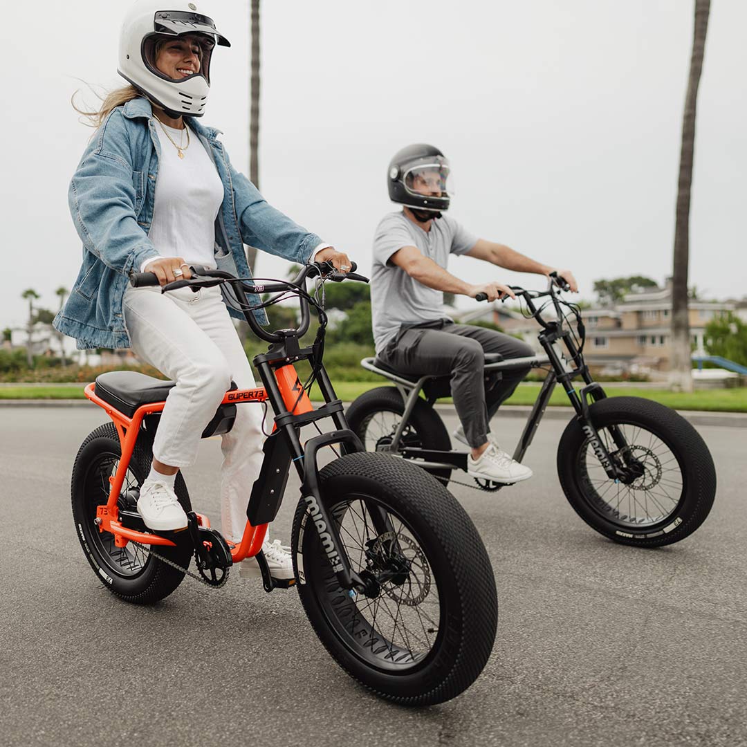 A man and woman riding Astro Orange and Metallic Aluminum SUPER73-Z Miami SE bikes.