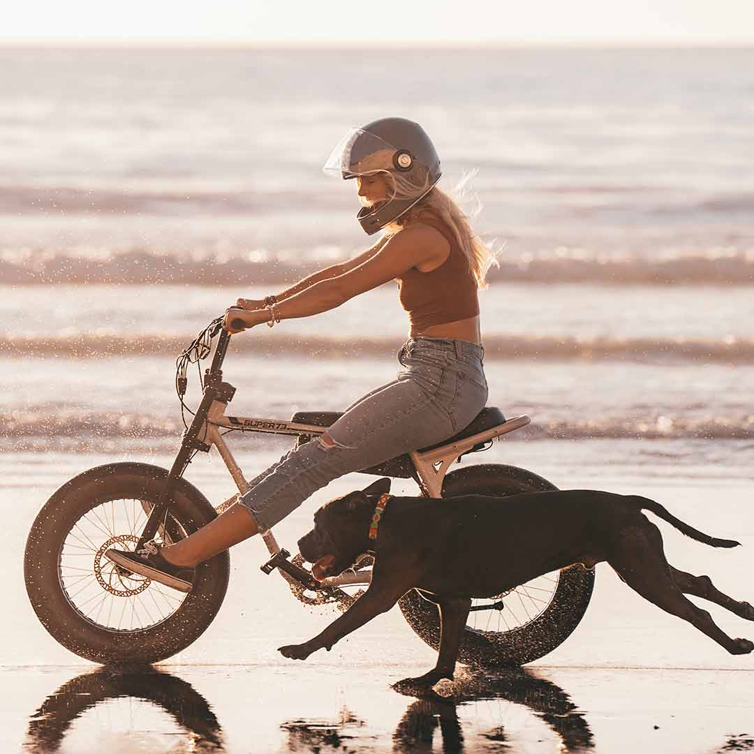 Young woman riding her super73 ebike z miami next to her dog on the beach at sunset