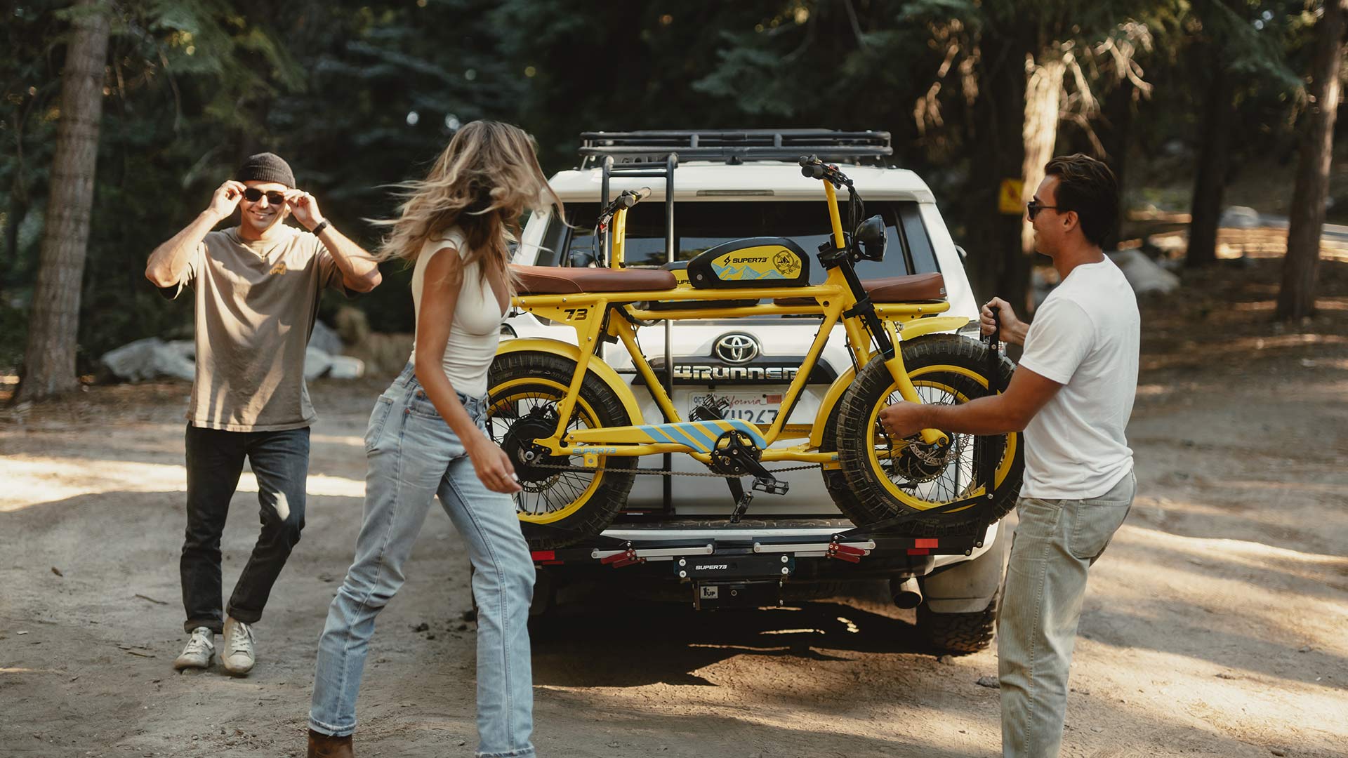 A man and woman loading a custom Pacifico x SUPER73-S2 bike onto the back of an SUV while another man stands to the side of the vehicle.