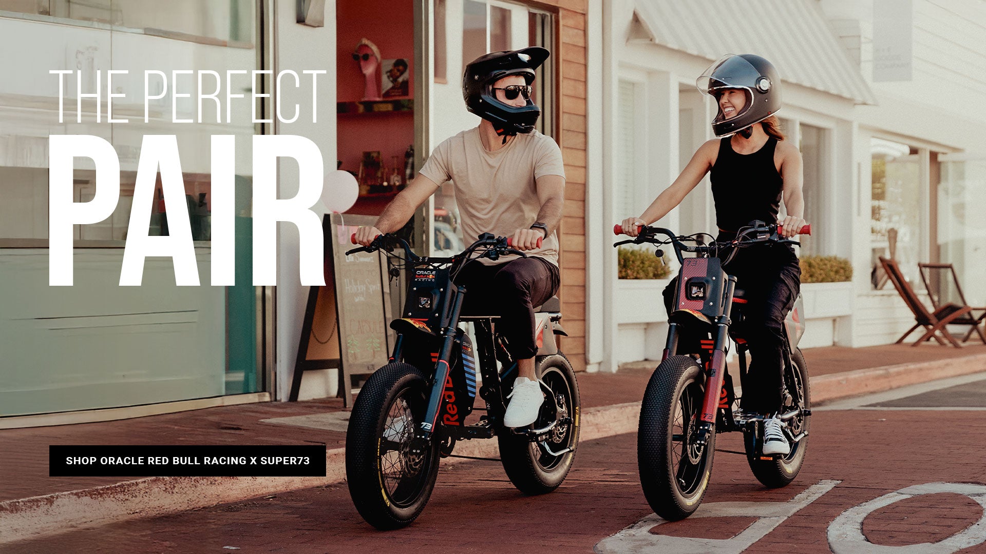 Lifestyle image of a man and woman in helmets riding the Oracle Red Bull Racing R Adventure Series and Z Adventure Series ebikes along a paved road.