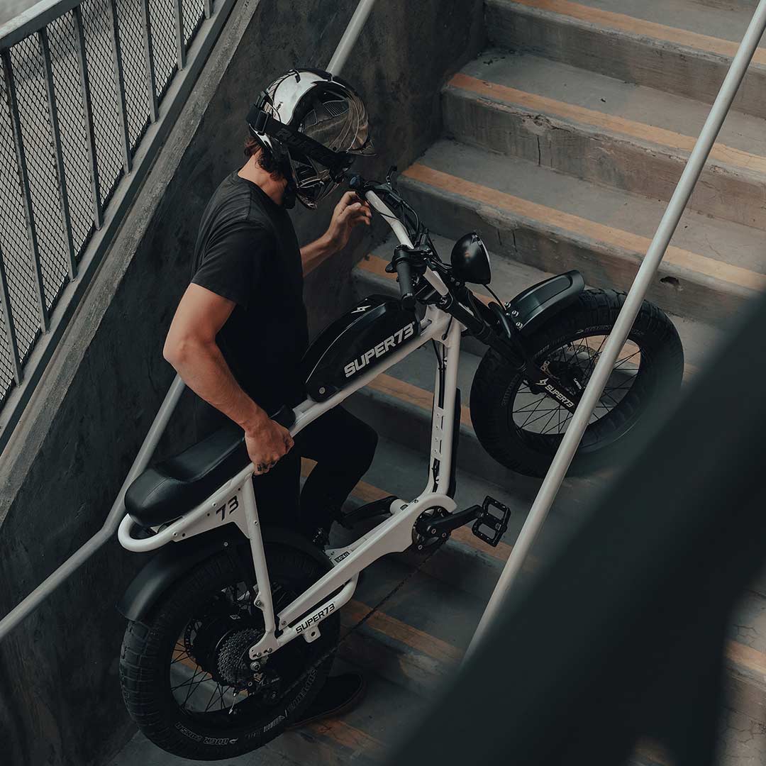 Man with a helmet on carrying his SUPER73 S2 ebike up a flight of stairs