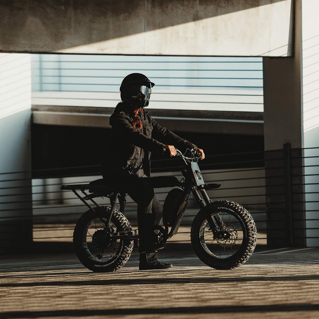 Image of a woman sitting on a SUPER73-S Blackout SE bike in a parking garage.