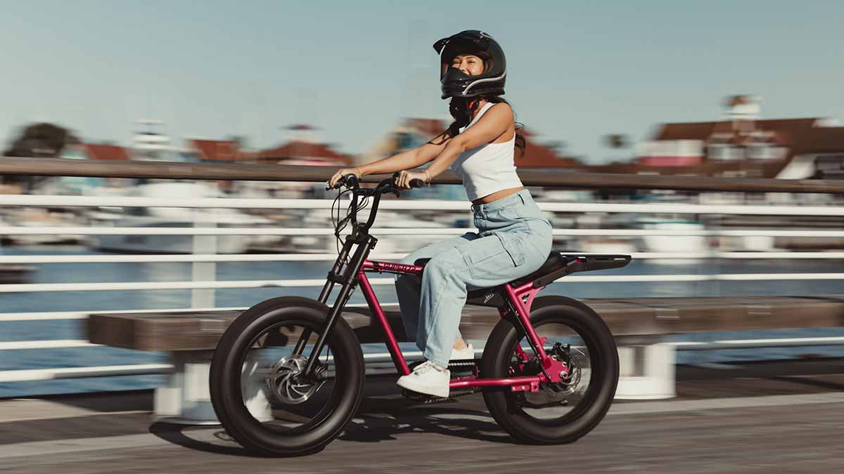 A Super73 Z Miami ebike cruising down the boardwalk with a young woman in a helmet
