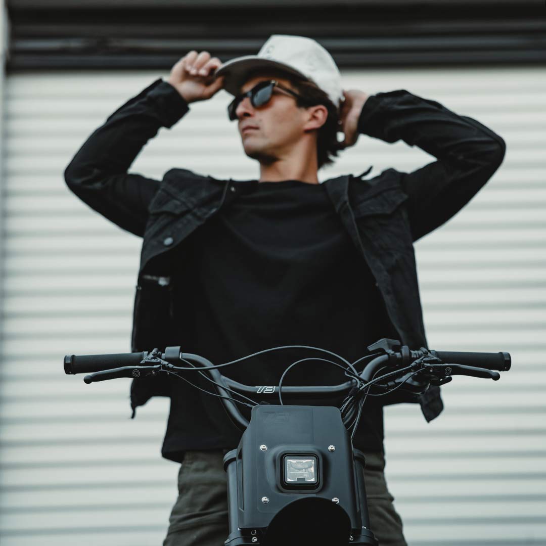 Image of a man sitting on a SUPER73-Z Blackout SE bike and adjusting his hat.