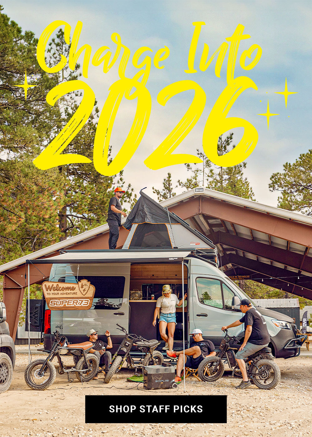 A group of people sit next to a camper van with several ebikes in the foreground. Text overlay reads "Charge into 2026" | Click to shop staff favorites.