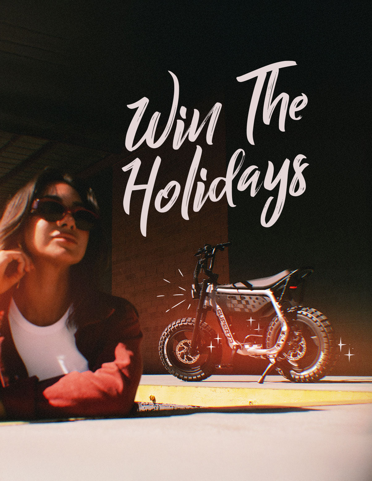 A woman wearing a red sweater and matching sunglasses stands in the foreground with a SUPER73-MZFT parked behind her. A text overlay reads "Win the Holidays"