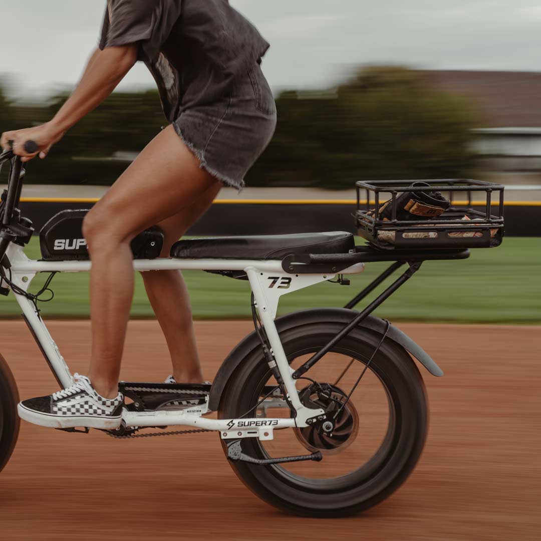 Lifestyle image of a woman riding a SUPER73 ebike with a cargo crate attached to the rear rack.