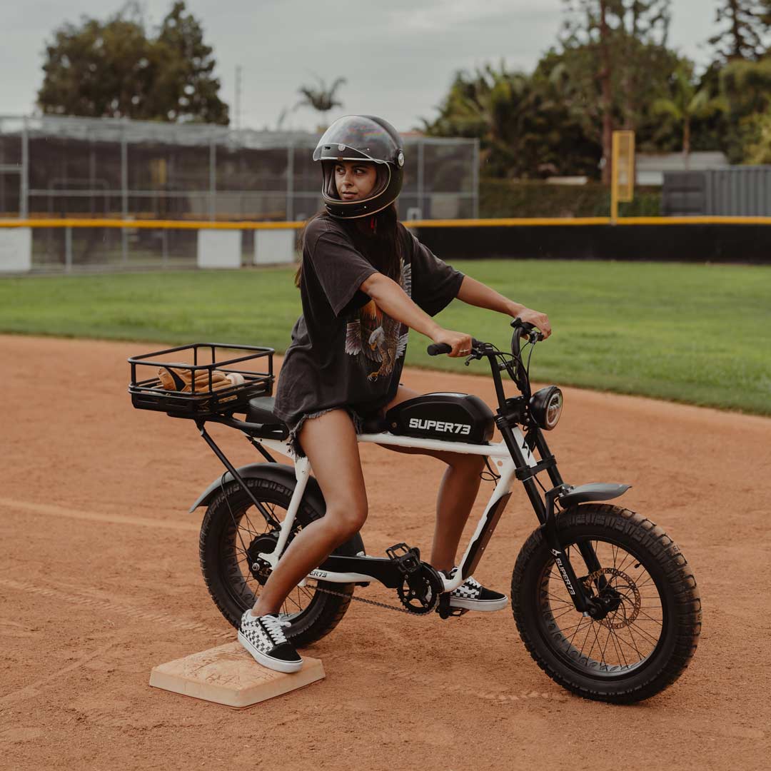 Lifestyle image of a woman sitting on a SUPER73 ebike with a cargo crate attached to the rear rack.