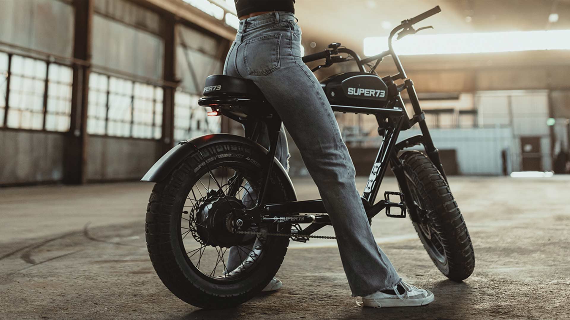 Rider in jeans sitting on Super73 S2 ebike in the middle of a warehouse