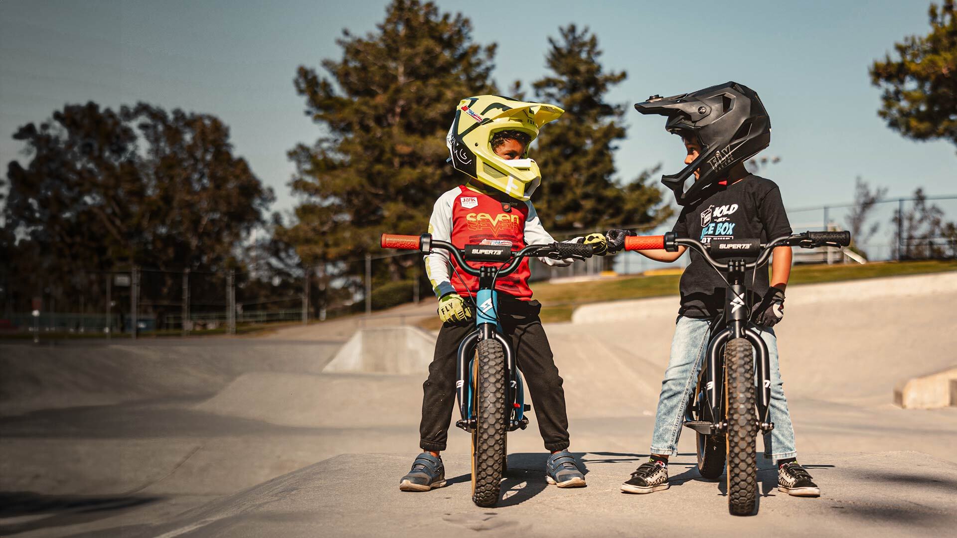 Two young kids sitting on SUPER73-K1D ebikes with helmets on