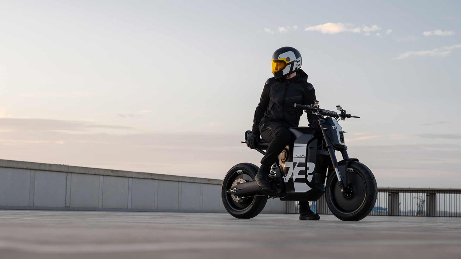 Lifestyle image of a male rider on the C1X looking out at the view while wearing a helmet.