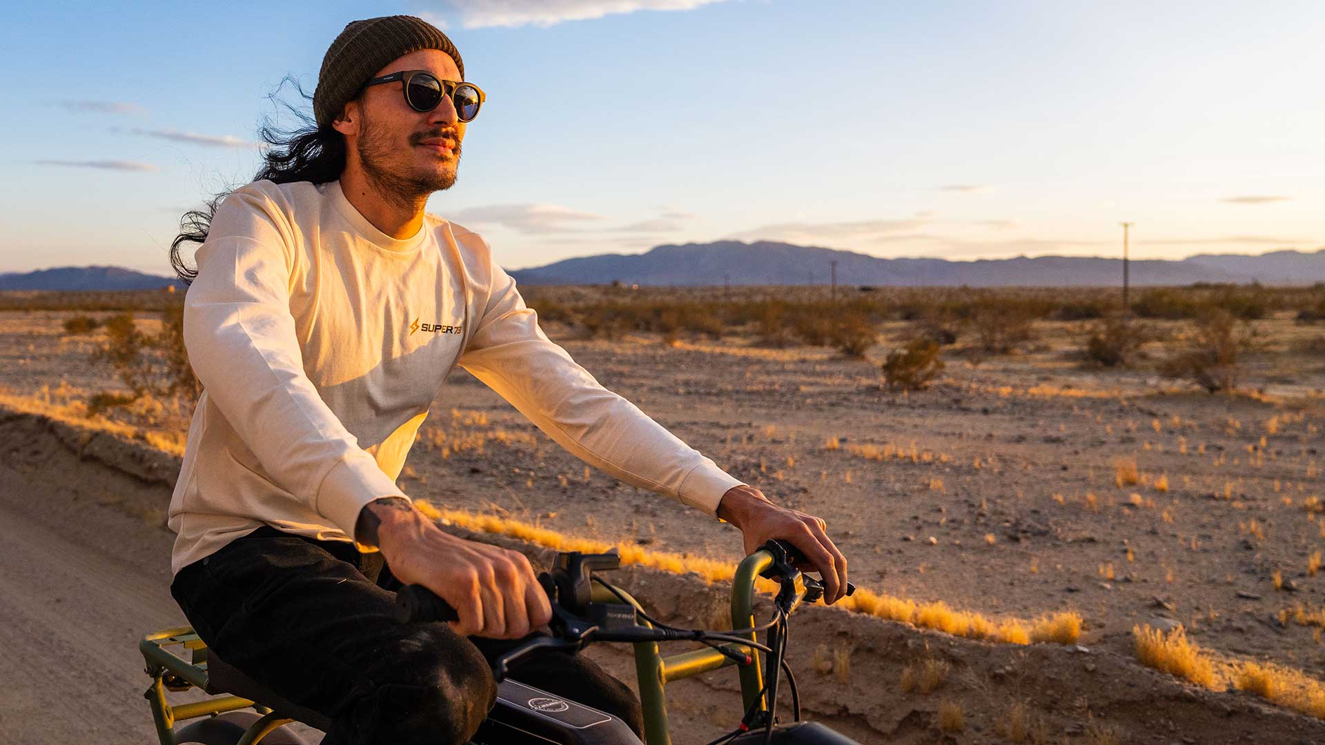 Closeup of rider wearing Super73 long sleeve t-shirt and riding Super73 ebike on a desert highway with wind in the hair