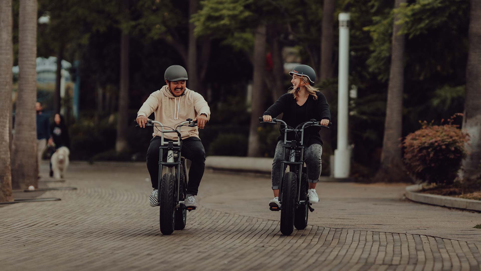 Two riders on Super73 ebikes passing through wooded park pathway