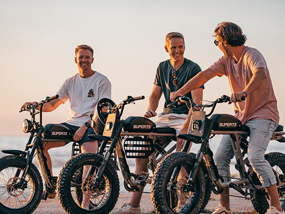 Three young men sitting on Super73 ebikes at the beach