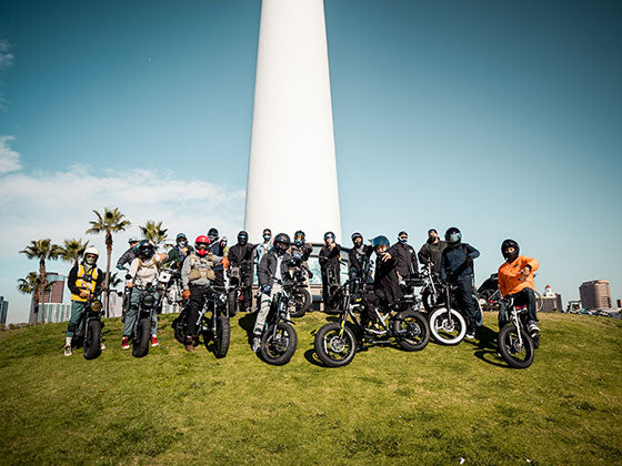 A large group of Super Squad members posing with their bikes in front of a lighthouse