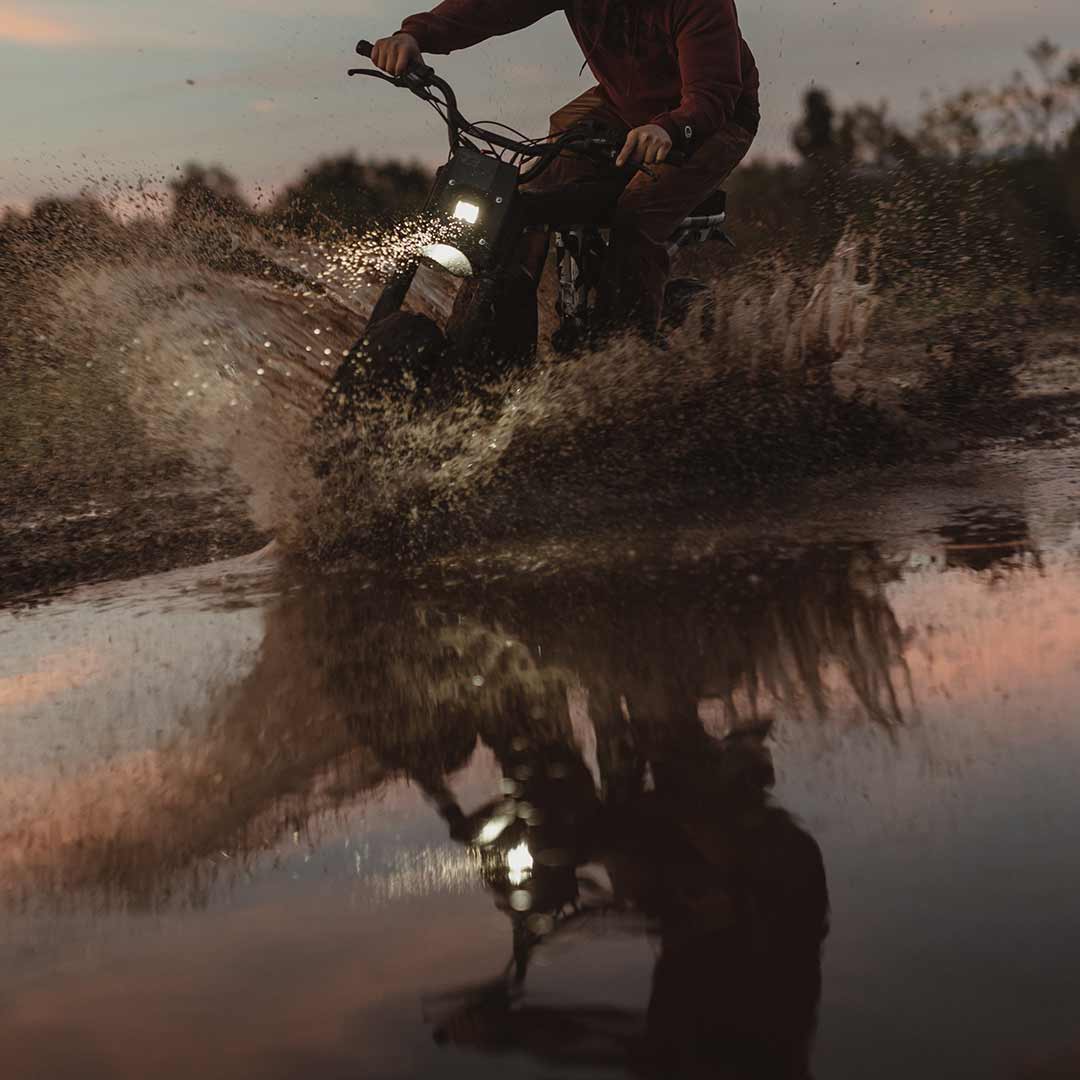 Lifestyle image of a rider riding the R Adventure through a pool of water at sunset and wearing a helmet.