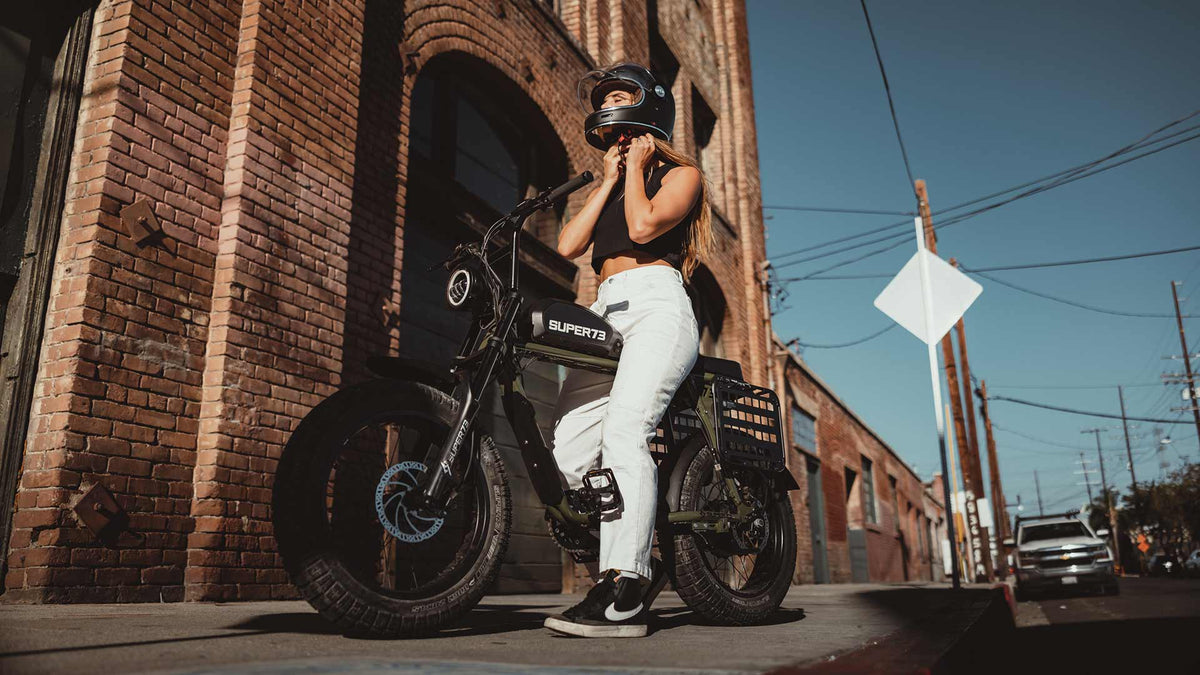 Rider sitting in front of brick building fastening helmet