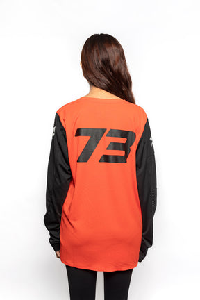 Female model back view of orange Premium long sleeve athletic moto hoon jersey.