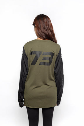 Female model back view of black and olive Premium long sleeve athletic moto hoon jersey.
