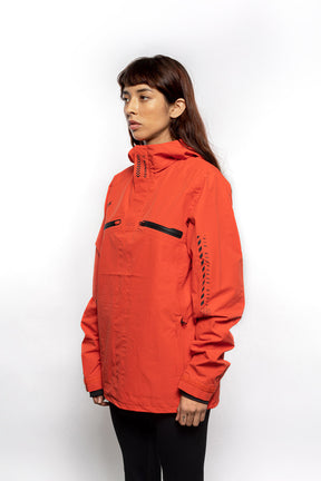 Side view of Female model wearing Vale Packable Anorak in blood orange colorway.